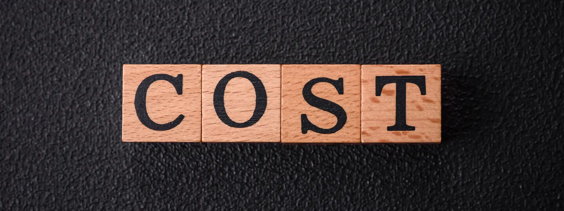 Image of wooden 'COST' blocks on a dark background, representing cost-effective mediation solutions at Summit Conflict Resolution.